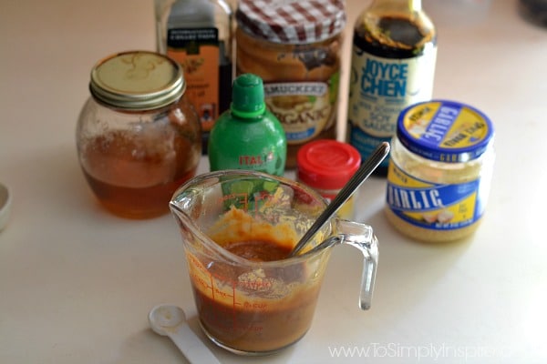 measuring cup with peanut butter and spoon with jars of peanut butter, garlic, honey, soy sauce and oil in the background