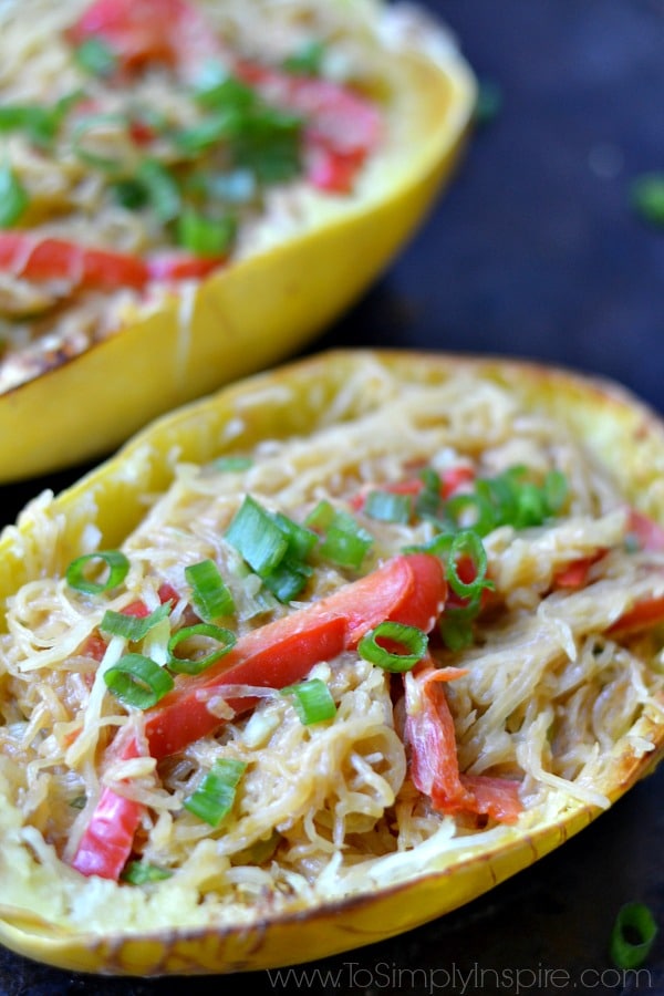 A close up of a spaghetti squash halves with red pepper slices and scallions