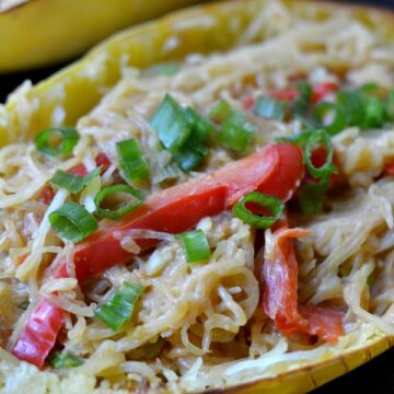 A close up of a spaghetti squash with red pepper slices and scallions