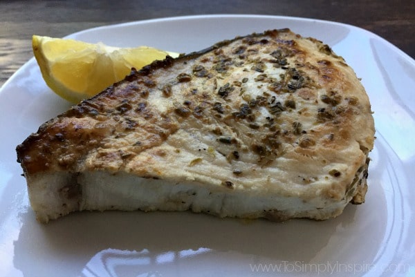 closeup of swordfish steak on a white plate with a lemon wedge