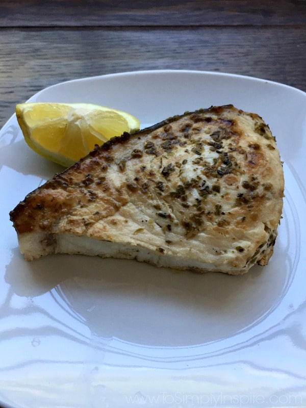 A piece of Swordfish on a white plate with a lemon wedge