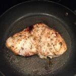 a swordfish steak cooking in a black pan