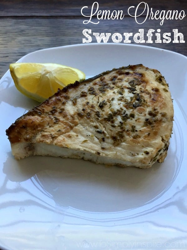 A piece of Swordfish on a white plate with a lemon wedge with text overlay Lemon Oregano Swordfish