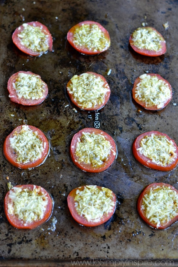 a full pan of sliced tomatoes on a baking sheet with parmesan cheese and pesto on top