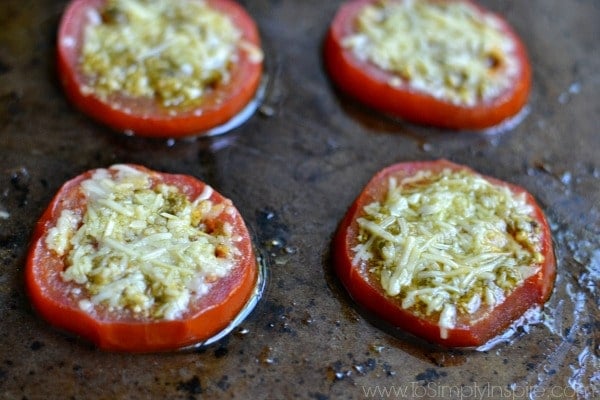 a closeup of sliced tomatoes on a baking sheet with parmesan cheese and pesto on top