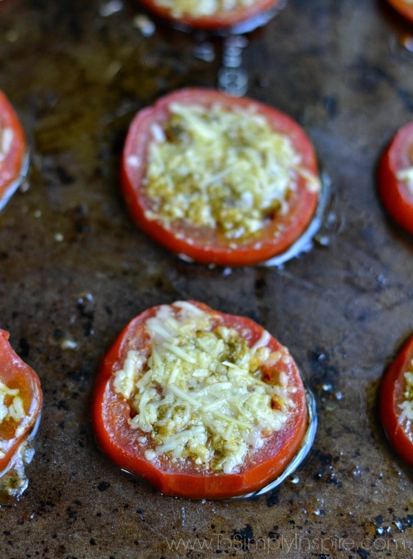 a closeup of sliced tomatoes on a baking sheet with parmesan cheese and pesto on top