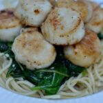 closeup of sautéed scallops over spinach and spaghetti noodles