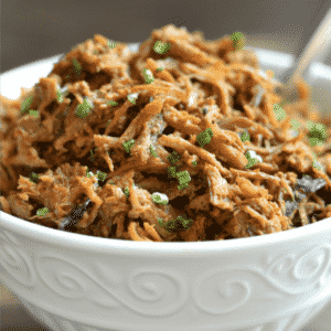 A close up of a bowl of shredded chicken topped with scallions