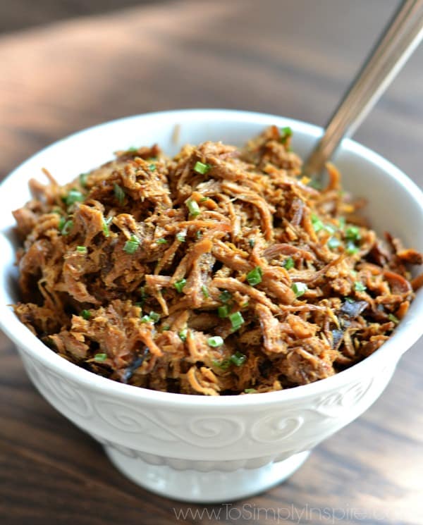 A close up of a white bowl of shredded chicken with honey garlic sauce topped with green onions