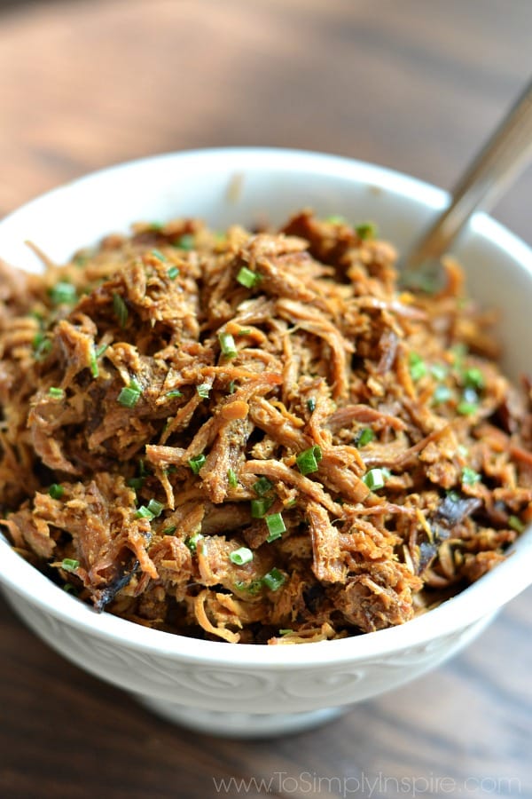 A close up of a white bowl of shredded chicken topped with green onions.