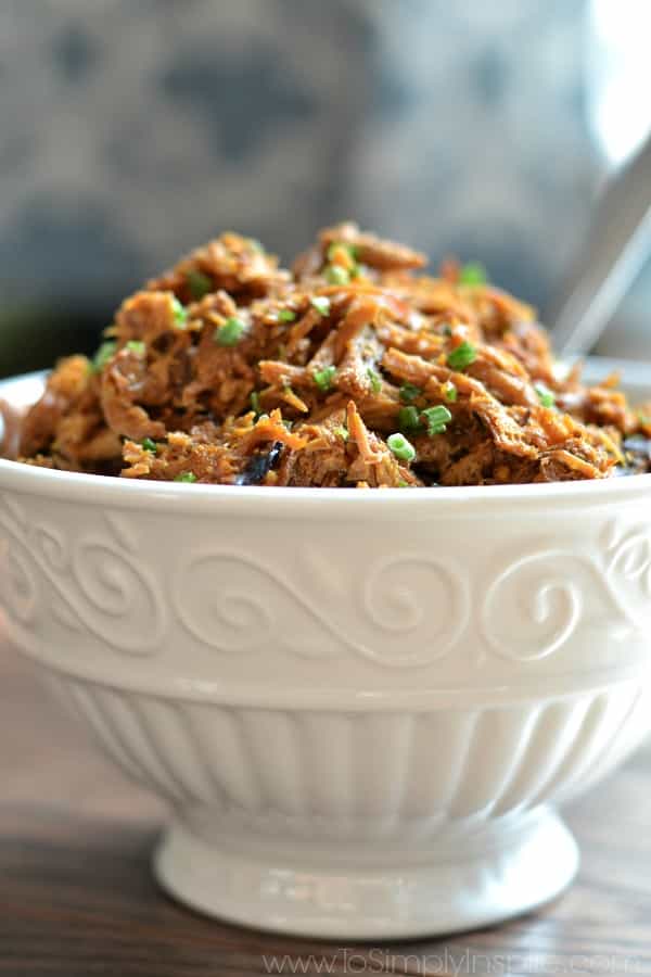 A close up of a shredded chicken with honey garlic sauce in a white bowl