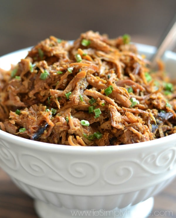 A close up of a white bowl of shredded chicken topped with green onions.