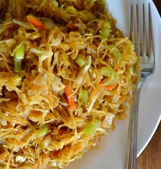 spaghetti squash with celery and shredded carrots on a white plate.