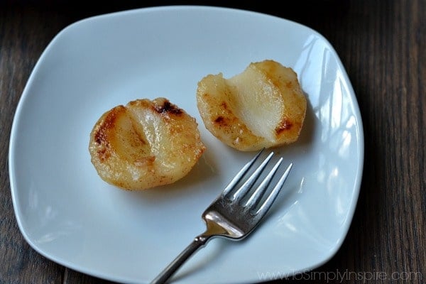 two baked pear halves on a white plate with a fork