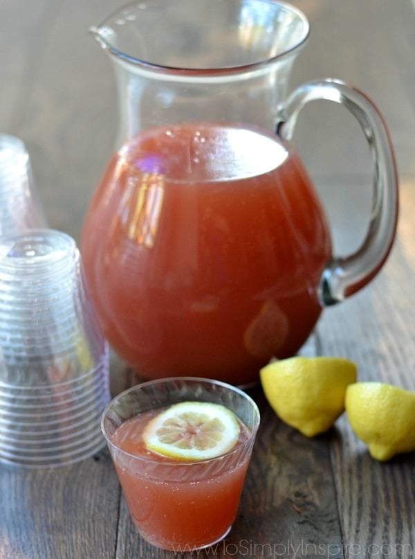 closeup of a glass pitcher of red punch with a stack of plastic cups beside and a cup full of punch in front