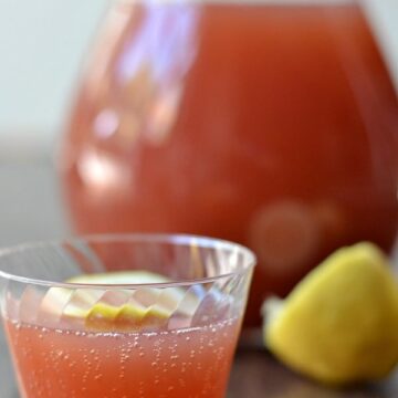 a plastic cup of red punch with a pitcher in the background