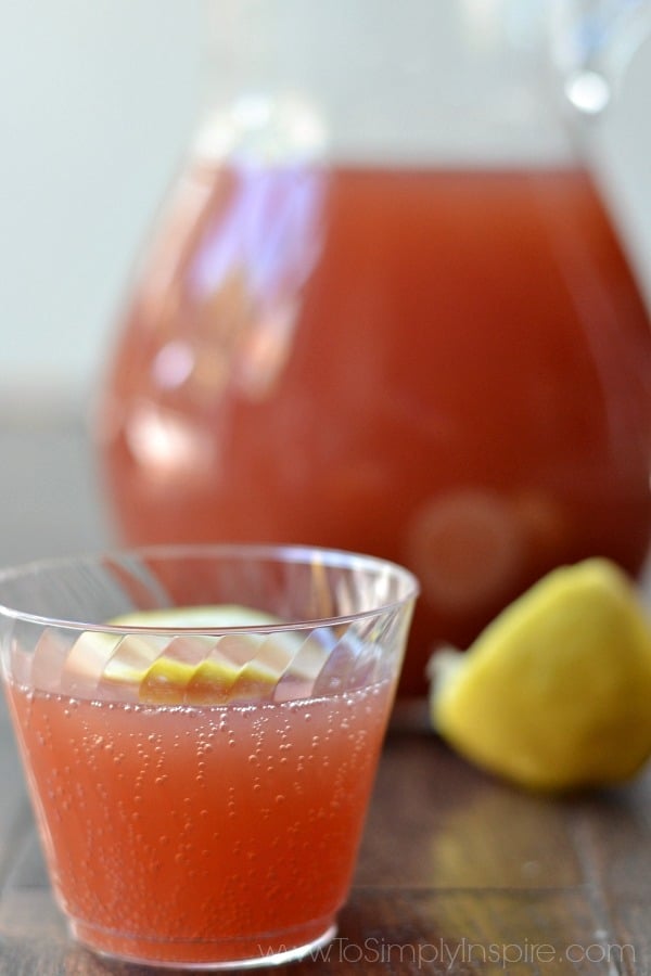 a plastic cup of red punch with a pitcher and half a lemon in the background