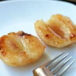 closeup of two baked pears halves drizzled with honey on a white plate.