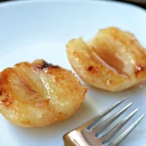 closeup of two baked pears halves drizzled with honey on a white plate.