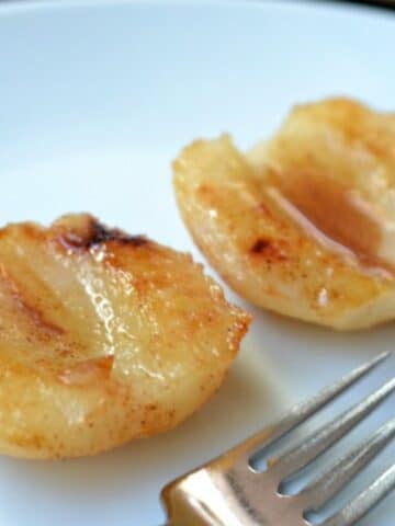 closeup of two baked pears halves drizzled with honey on a white plate.