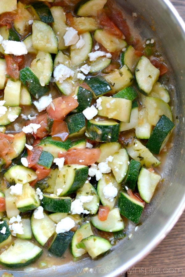 A closeup of zucchini, feta cheese and diced tomatoes in a bowl