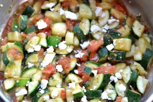 closeup of zucchini, feta cheese and diced tomatoes in a pan