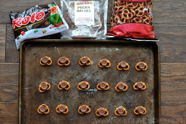 a bunch of pretzel knots topped with a rolo and a pecan half on a baking sheet surrounded by ingredients