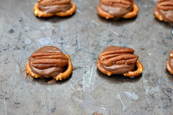 four pretzel knots topped with a rolo and a pecan half on a baking sheet