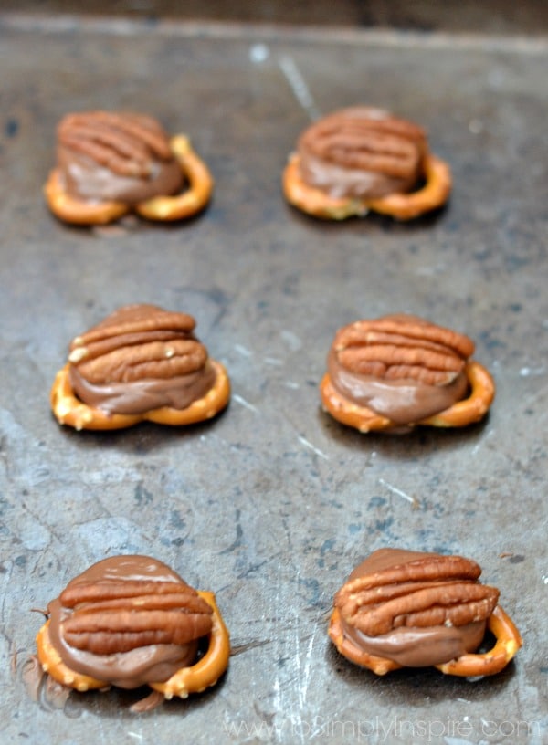 a bunch of pretzel knots topped with rolo candies and a pecan half on a baking sheet