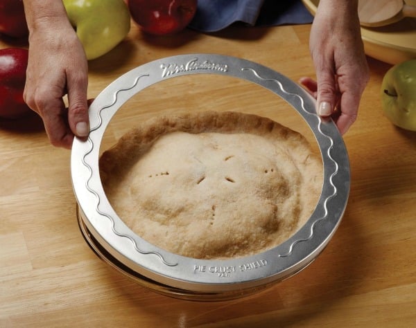 A persons hands holding a silver pie ring over a pie