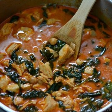 A closeup of a bowl of soup with chickpeas and spinach with a wooden spoon