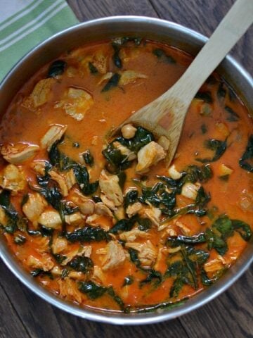 closeup of Curry Chicken and Chickpeas recipe with spinach in a stainless steel pot with wooden spoon