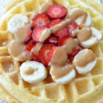 Closeup of Protein Waffle on a white plate topped with sliced strawberries and bananas drizzled with peanut butter.