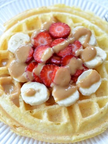 Closeup of Protein Waffle on a white plate topped with sliced strawberries and bananas drizzled with peanut butter.