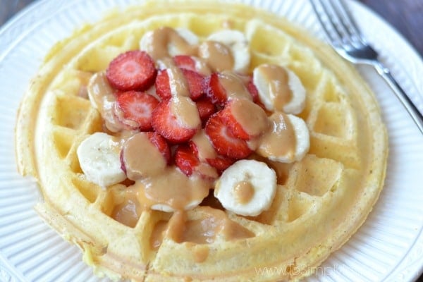 Closeup of Protein Waffle on a white plate topped with sliced strawberries and bananas drizzled with peanut butter.