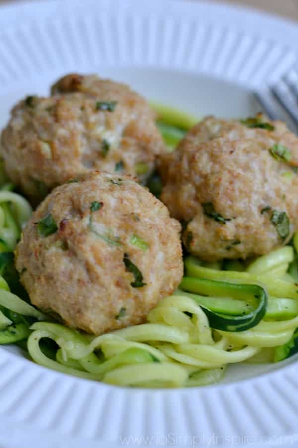 three Asian Turkey Meatballs over zucchini noodles on a white plate with a fork
