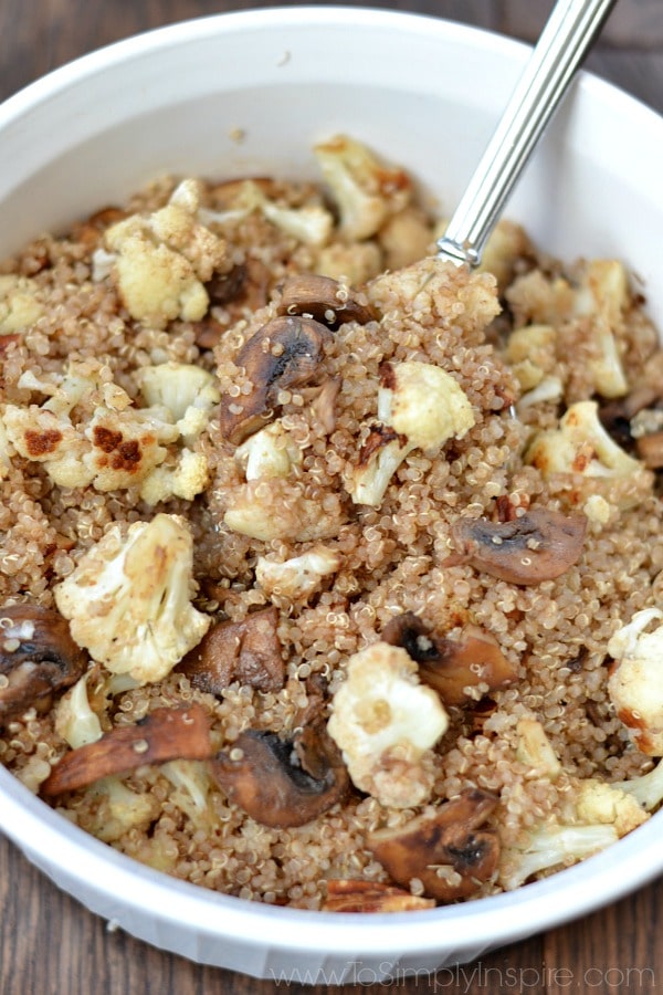 A closeup of a bowl of quinoa, cauliflower and mushrooms in a white bowl with a spoon