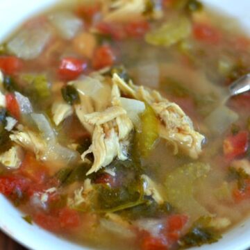 Closeup of chicken soup with tomatoes and cilantro in a white bowl