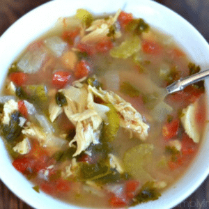 A bowl of Cilantro Lime Chicken Soup with shredded chicken, diced tomatoes, celery, onions, fresh herbs, and a spoon.