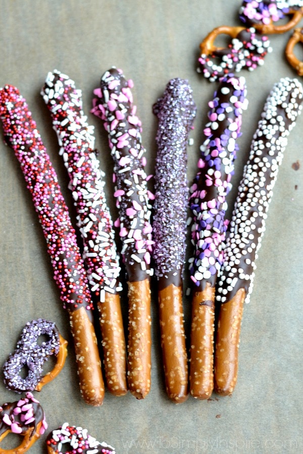 Six Chocolate Covered Pretzel rods covered in valentines sprinkles laying on parchment paper  