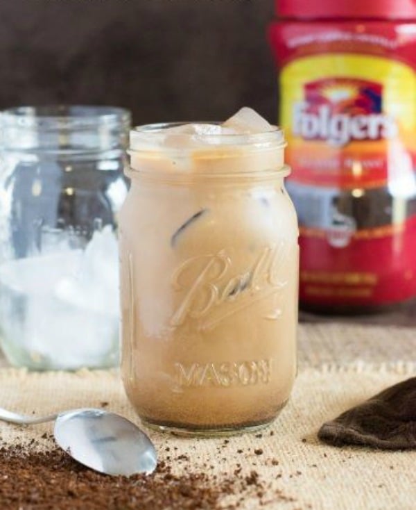 A mason jar with Iced coffee with and empty mug of ice in background