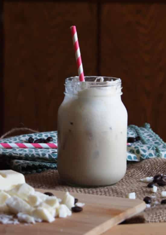 iced white chocolate coffee in a mason jar with a red and white straw and a wooden background