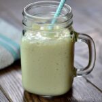 A glass mug with mango banana smoothie on a wood table