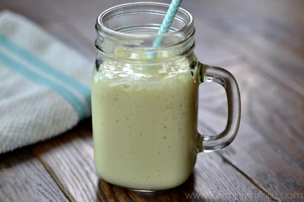 A closeup of a glass mug with mango banana smoothie with a light blue straw on a wood table