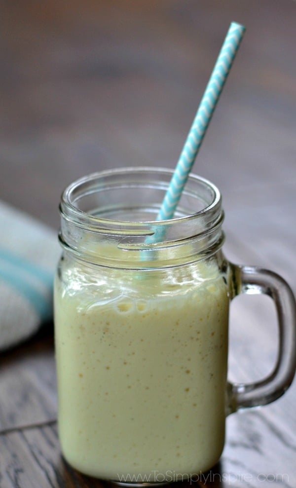 A closeup of a glass mug with mango banana smoothie with a light blue straw