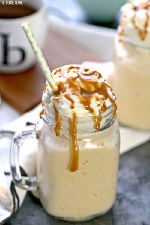 a glass mug of iced coffee with caramel sauce dripping over whipped cream