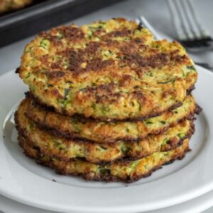 stack of four zucchini fritters on a white plate