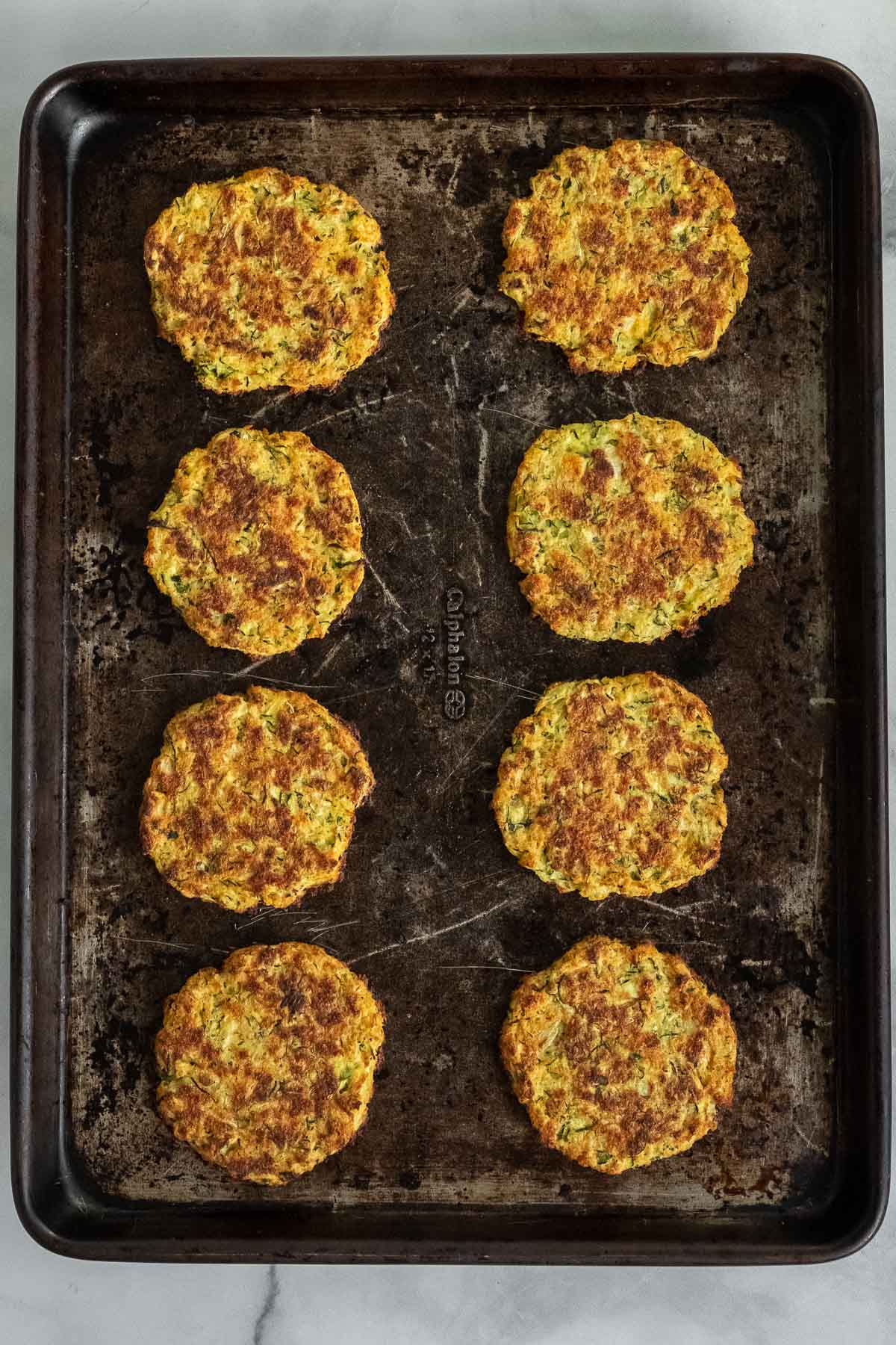 eight cooked zucchini fritters on a baking sheet