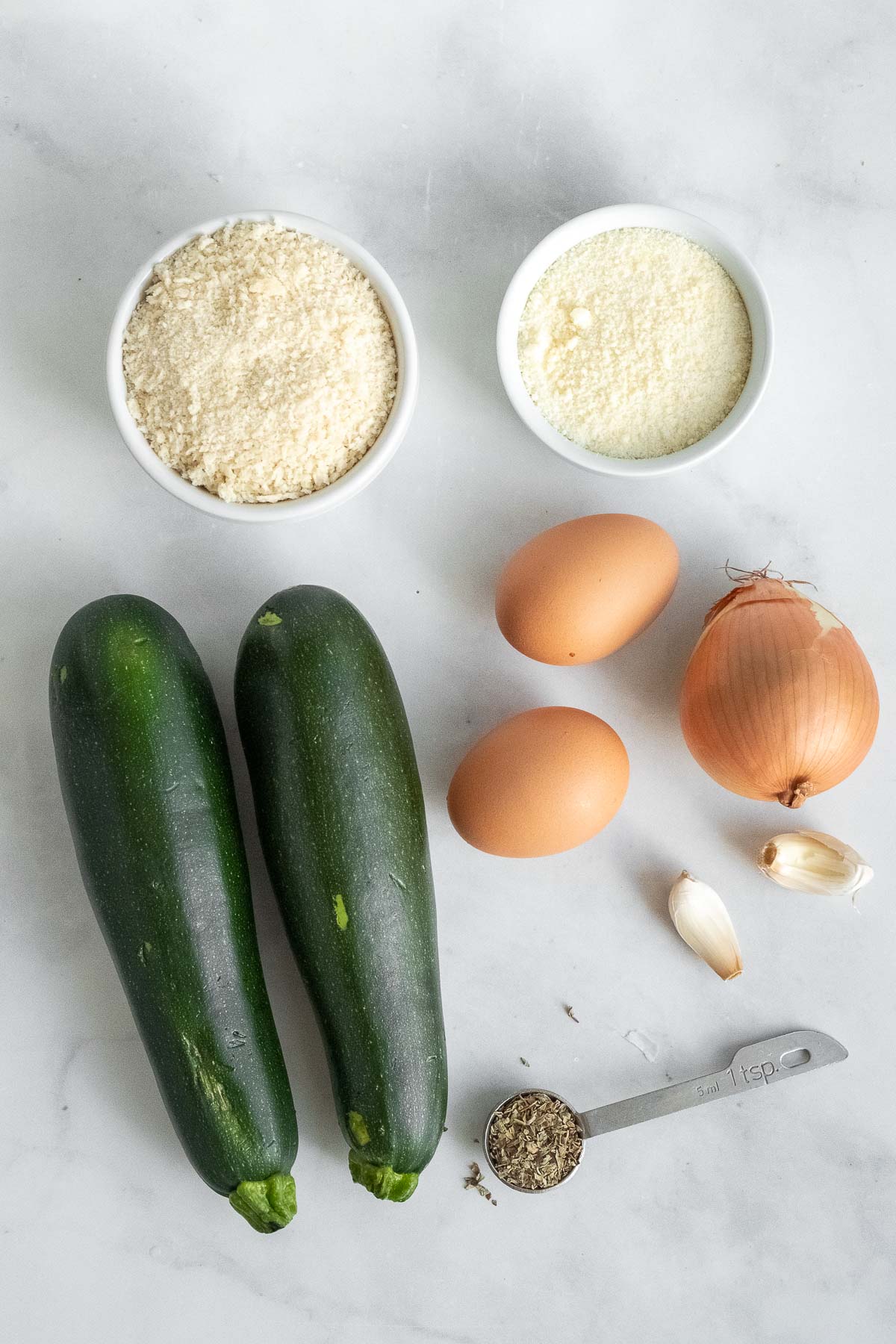 two zucchini, 2 eggs, one onion, bowl of breadcrumbs, bowl of parmesan cheese