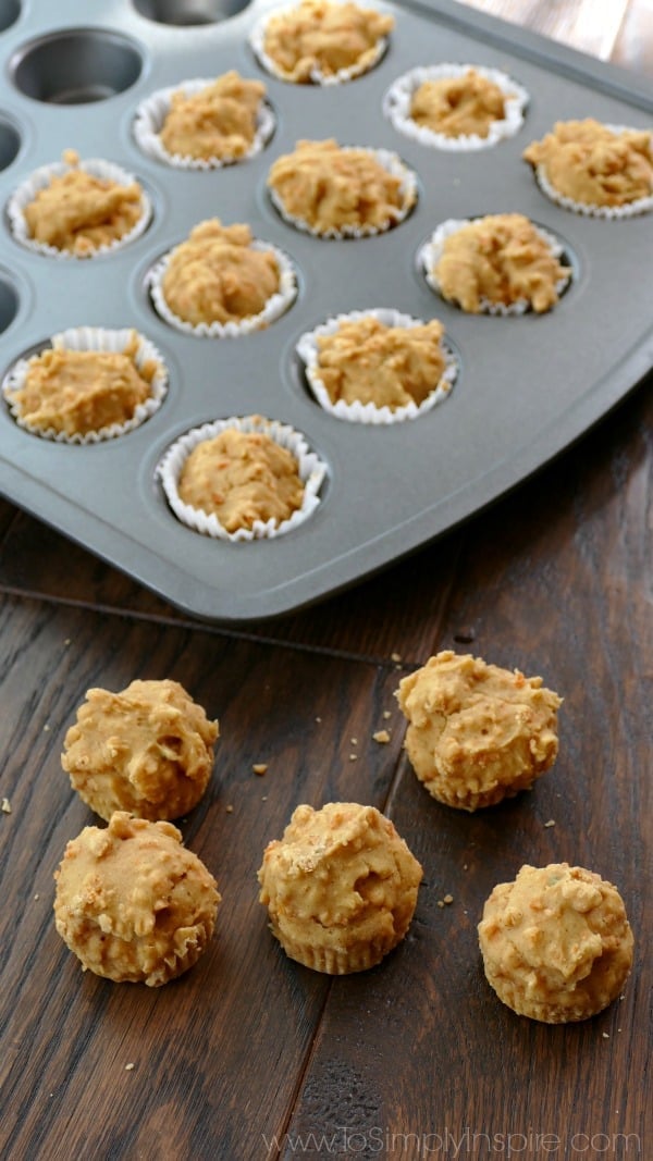 five mini carrot cake muffins on a wood table with a muffin tin in the background